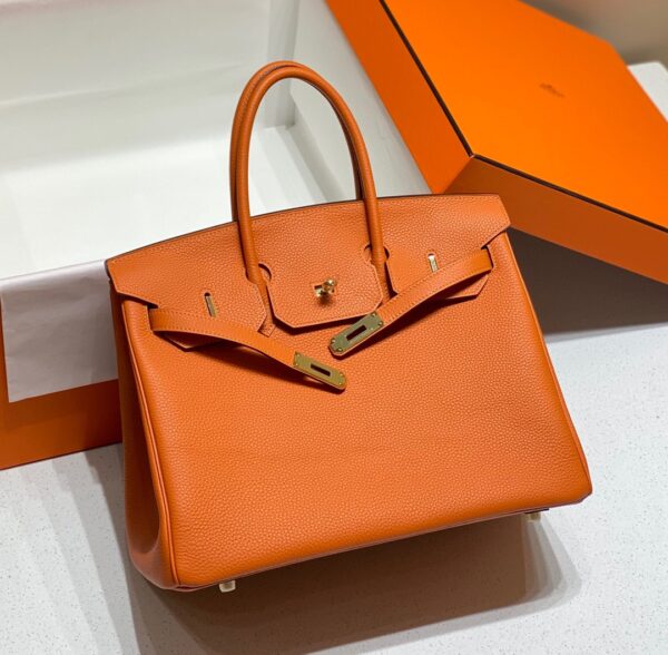 Birkin. Authentic quality luxury bag crafted in genuine leather comes with authenticity card, dust bag and gift bag. Exquisite Craftsmanship and Timeless Elegance: Discover the Allure of the Birkin Bag Large Leather Top Handle. Designed with the actress Jane Birkin in mind, the Birkin bag is a contemporary development of the Kelly bag. Created based on Jane’s suggestions, it was architected to be more significant to fit modern women’s fast-paced life, with several minor yet outstanding adaptations, such as the elongated top handles. The French Birkin 30 bag is a classic touch of elegance to your look! The accessory features a trapeze body, a pebbled leather texture, a hanging key fob, gold-tone hardware, round top handles, a padlock fastening detail, a foldover top with twist-lock closure, a front center logo stamp, an internal zipped pocket, and purse feet.