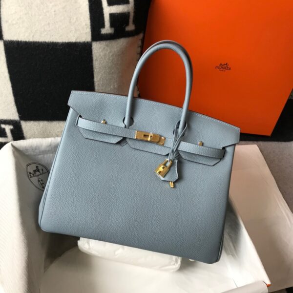 Birkin. Authentic quality luxury bag crafted in genuine leather comes with authenticity card, dust bag and gift bag. Exquisite Craftsmanship and Timeless Elegance: Discover the Allure of the Birkin Bag Large Leather Top Handle. Designed with the actress Jane Birkin in mind, the Birkin bag is a contemporary development of the Kelly bag. Created based on Jane’s suggestions, it was architected to be more significant to fit modern women’s fast-paced life, with several minor yet outstanding adaptations, such as the elongated top handles. The French Birkin 30 bag is a classic touch of elegance to your look! The accessory features a trapeze body, a pebbled leather texture, a hanging key fob, gold-tone hardware, round top handles, a padlock fastening detail, a foldover top with twist-lock closure, a front center logo stamp, an internal zipped pocket, and purse feet.