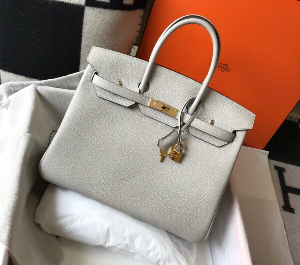 Birkin. Authentic quality luxury bag crafted in genuine leather comes with authenticity card, dust bag and gift bag. Exquisite Craftsmanship and Timeless Elegance: Discover the Allure of the Birkin Bag Large Leather Top Handle. Designed with the actress Jane Birkin in mind, the Birkin bag is a contemporary development of the Kelly bag. Created based on Jane’s suggestions, it was architected to be more significant to fit modern women’s fast-paced life, with several minor yet outstanding adaptations, such as the elongated top handles. The French Birkin 30 bag is a classic touch of elegance to your look! The accessory features a trapeze body, a pebbled leather texture, a hanging key fob, gold-tone hardware, round top handles, a padlock fastening detail, a foldover top with twist-lock closure, a front center logo stamp, an internal zipped pocket, and purse feet.