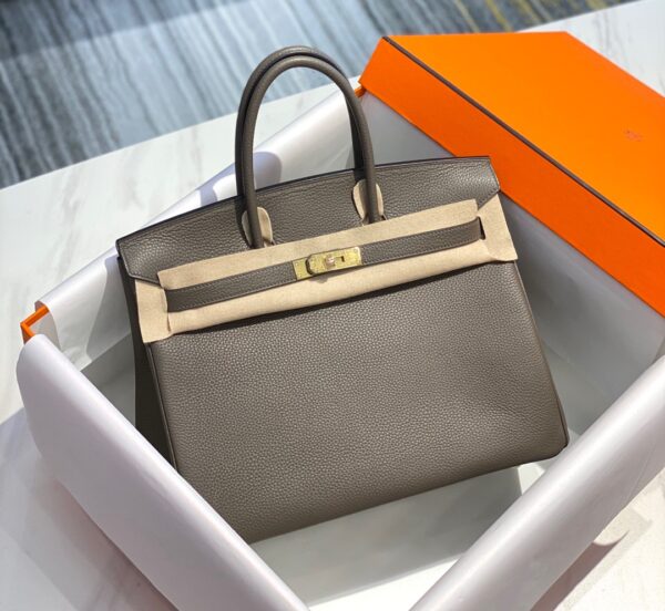 Birkin. Authentic quality luxury bag crafted in genuine leather comes with authenticity card, dust bag and gift bag. Exquisite Craftsmanship and Timeless Elegance: Discover the Allure of the Birkin Bag Large Leather Top Handle. Designed with the actress Jane Birkin in mind, the Birkin bag is a contemporary development of the Kelly bag. Created based on Jane’s suggestions, it was architected to be more significant to fit modern women’s fast-paced life, with several minor yet outstanding adaptations, such as the elongated top handles. The French Birkin 30 bag is a classic touch of elegance to your look! The accessory features a trapeze body, a pebbled leather texture, a hanging key fob, gold-tone hardware, round top handles, a padlock fastening detail, a foldover top with twist-lock closure, a front center logo stamp, an internal zipped pocket, and purse feet.