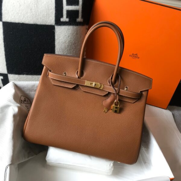 Birkin. Authentic quality luxury bag crafted in genuine leather comes with authenticity card, dust bag and gift bag. Exquisite Craftsmanship and Timeless Elegance: Discover the Allure of the Birkin Bag Large Leather Top Handle. Designed with the actress Jane Birkin in mind, the Birkin bag is a contemporary development of the Kelly bag. Created based on Jane’s suggestions, it was architected to be more significant to fit modern women’s fast-paced life, with several minor yet outstanding adaptations, such as the elongated top handles. The French Birkin 30 bag is a classic touch of elegance to your look! The accessory features a trapeze body, a pebbled leather texture, a hanging key fob, gold-tone hardware, round top handles, a padlock fastening detail, a foldover top with twist-lock closure, a front center logo stamp, an internal zipped pocket, and purse feet.