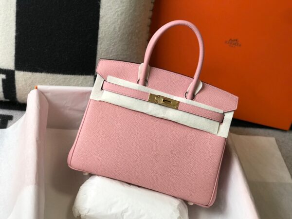 Birkin. Authentic quality luxury bag crafted in genuine leather comes with authenticity card, dust bag and gift bag. Exquisite Craftsmanship and Timeless Elegance: Discover the Allure of the Birkin Bag Large Leather Top Handle. Designed with the actress Jane Birkin in mind, the Birkin bag is a contemporary development of the Kelly bag. Created based on Jane’s suggestions, it was architected to be more significant to fit modern women’s fast-paced life, with several minor yet outstanding adaptations, such as the elongated top handles. The French Birkin 30 bag is a classic touch of elegance to your look! The accessory features a trapeze body, a pebbled leather texture, a hanging key fob, gold-tone hardware, round top handles, a padlock fastening detail, a foldover top with twist-lock closure, a front center logo stamp, an internal zipped pocket, and purse feet.