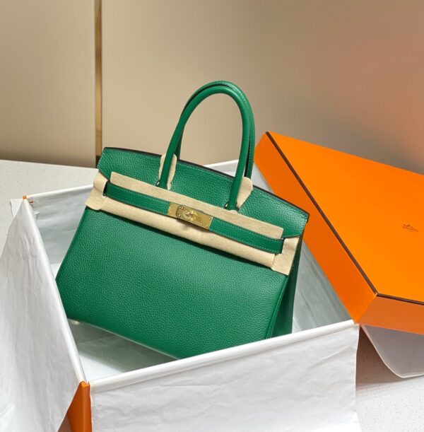Birkin. Authentic quality luxury bag crafted in genuine leather comes with authenticity card, dust bag and gift bag. Exquisite Craftsmanship and Timeless Elegance: Discover the Allure of the Birkin Bag Large Leather Top Handle. Designed with the actress Jane Birkin in mind, the Birkin bag is a contemporary development of the Kelly bag. Created based on Jane’s suggestions, it was architected to be more significant to fit modern women’s fast-paced life, with several minor yet outstanding adaptations, such as the elongated top handles. The French Birkin 30 bag is a classic touch of elegance to your look! The accessory features a trapeze body, a pebbled leather texture, a hanging key fob, gold-tone hardware, round top handles, a padlock fastening detail, a foldover top with twist-lock closure, a front center logo stamp, an internal zipped pocket, and purse feet.