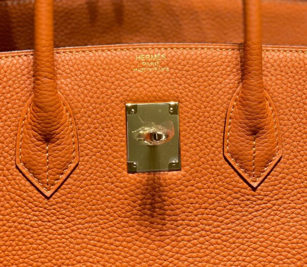 Birkin. Authentic quality luxury bag crafted in genuine leather comes with authenticity card, dust bag and gift bag. Exquisite Craftsmanship and Timeless Elegance: Discover the Allure of the Birkin Bag Large Leather Top Handle. Designed with the actress Jane Birkin in mind, the Birkin bag is a contemporary development of the Kelly bag. Created based on Jane’s suggestions, it was architected to be more significant to fit modern women’s fast-paced life, with several minor yet outstanding adaptations, such as the elongated top handles. The French Birkin 30 bag is a classic touch of elegance to your look! The accessory features a trapeze body, a pebbled leather texture, a hanging key fob, gold-tone hardware, round top handles, a padlock fastening detail, a foldover top with twist-lock closure, a front center logo stamp, an internal zipped pocket, and purse feet.