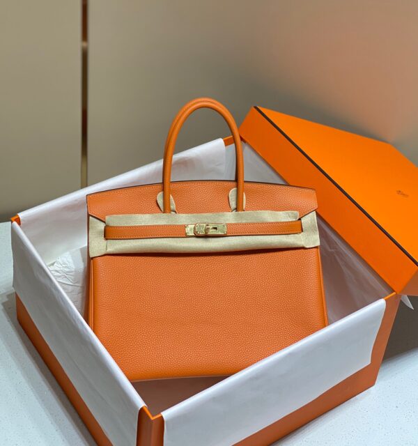 Birkin. Authentic quality luxury bag crafted in genuine leather comes with authenticity card, dust bag and gift bag. Exquisite Craftsmanship and Timeless Elegance: Discover the Allure of the Birkin Bag Large Leather Top Handle. Designed with the actress Jane Birkin in mind, the Birkin bag is a contemporary development of the Kelly bag. Created based on Jane’s suggestions, it was architected to be more significant to fit modern women’s fast-paced life, with several minor yet outstanding adaptations, such as the elongated top handles. The French Birkin 30 bag is a classic touch of elegance to your look! The accessory features a trapeze body, a pebbled leather texture, a hanging key fob, gold-tone hardware, round top handles, a padlock fastening detail, a foldover top with twist-lock closure, a front center logo stamp, an internal zipped pocket, and purse feet.
